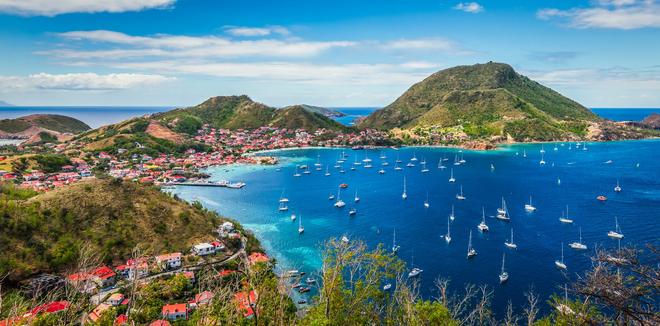 Green hilly coastline of Guadelope island with a small town and boats.