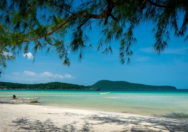 Boat on the white beach on Koh Rong island (Cambodia) in sunny weather with a view of the forested hills in the distance.