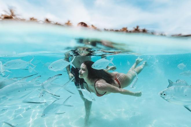 A girl swimming among fish in crystal-clear water, Maldives