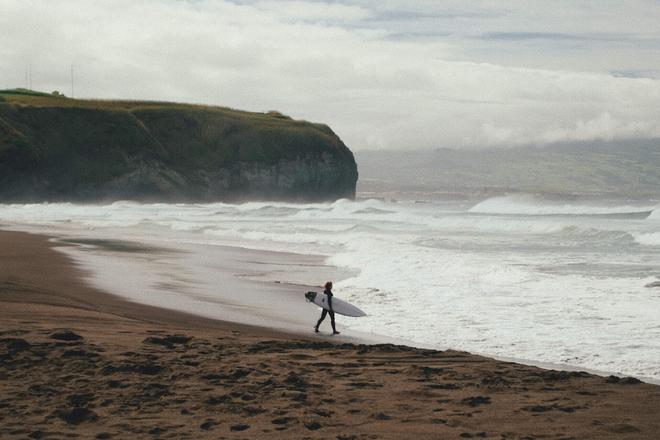 A girl carying a surf on a beach in Madeira