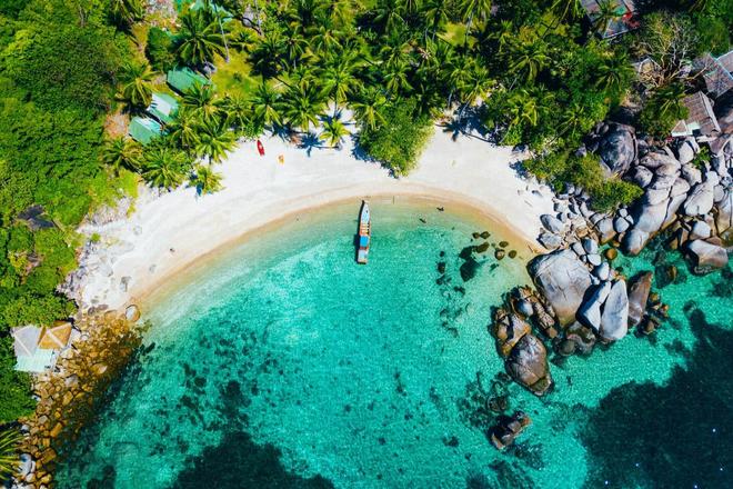 A boat, turquoise sea and beach surrounded by trees and houses in Koh Phangan