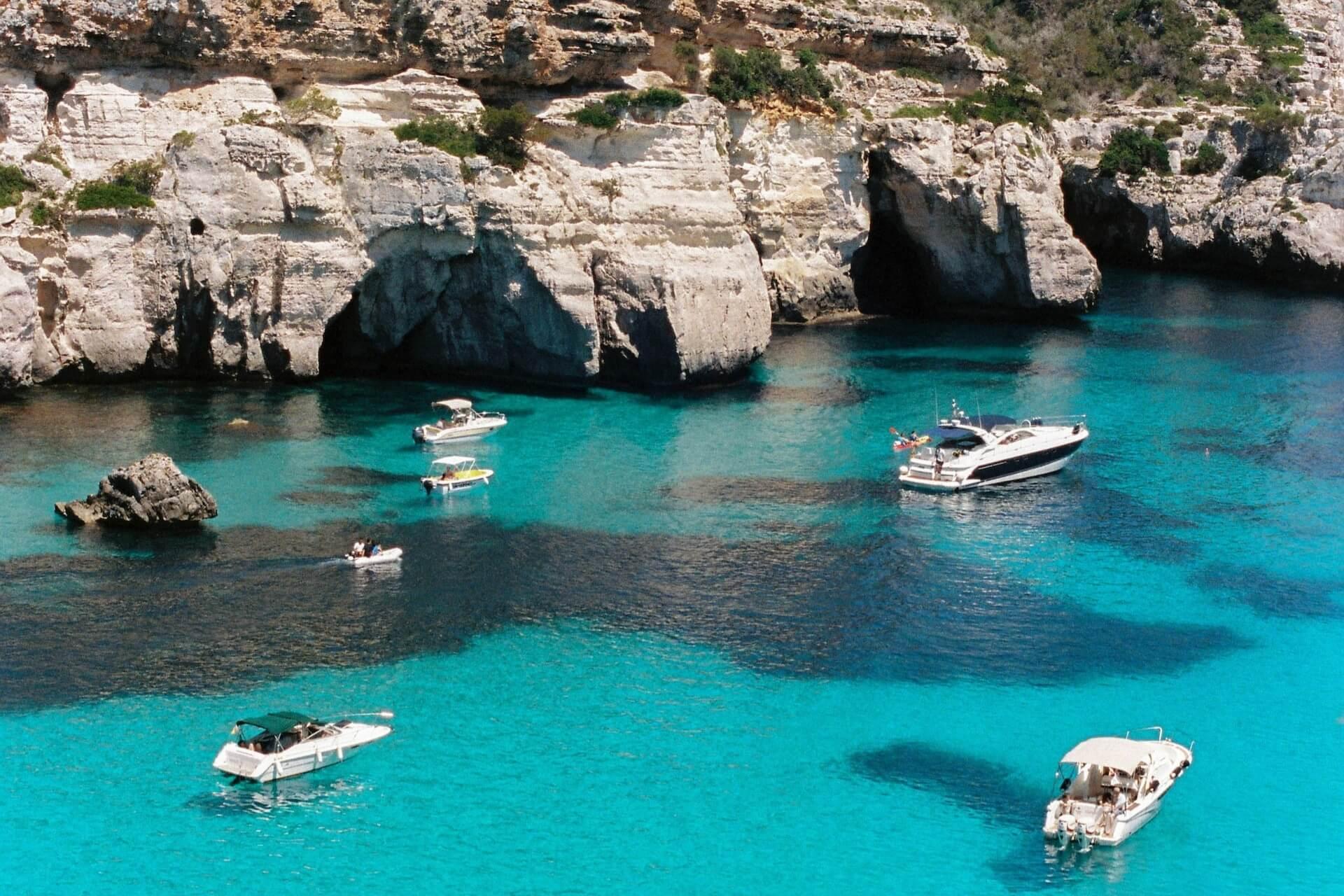 View of boats on a sea and rocky formations in the background in Menorca