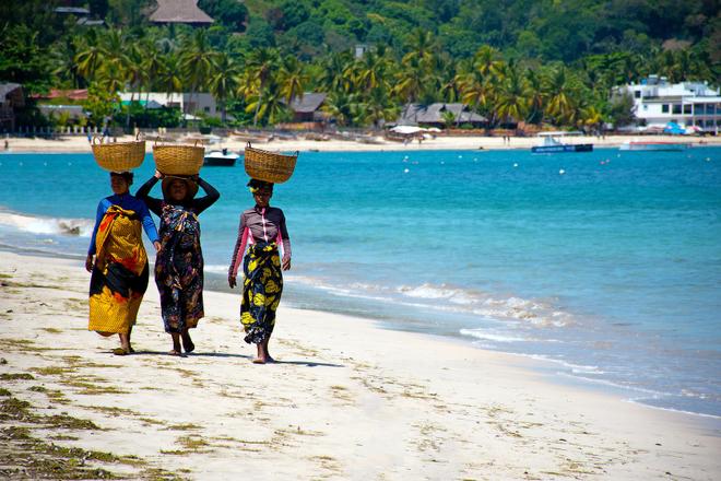 Madagascar: three women on the beach carrying baskets on their heads.
