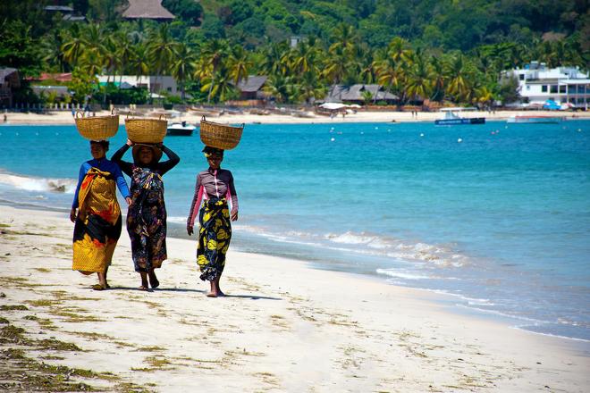 Madagascar: three women on the beach carrying baskets on their heads.