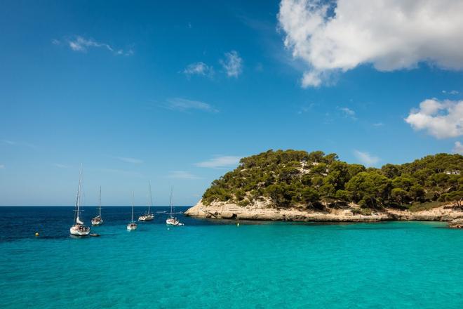View of boats, sea and a part of an island along with Cala Mitjana bay in Menorca