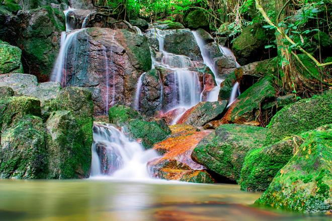 Waterfall in the moss-covered rocks with a pond on the island of Koh Samui in Southeast Thailand.