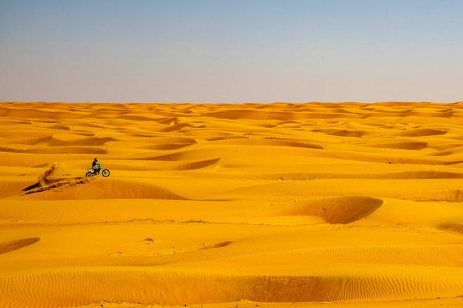 A person riding a pitbike through sand dunes