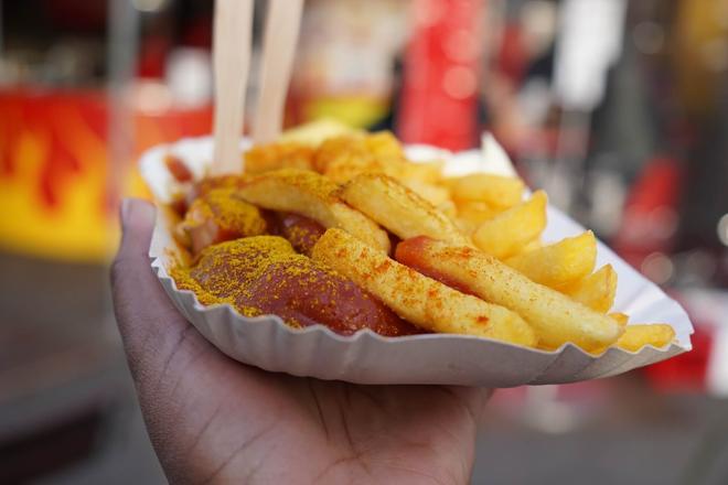 A hand holding a plate with currywurst on it in Berlin