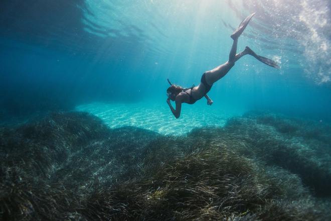 Woman wearing snorkeling gear diving to the bottom of the ocean in Menorca