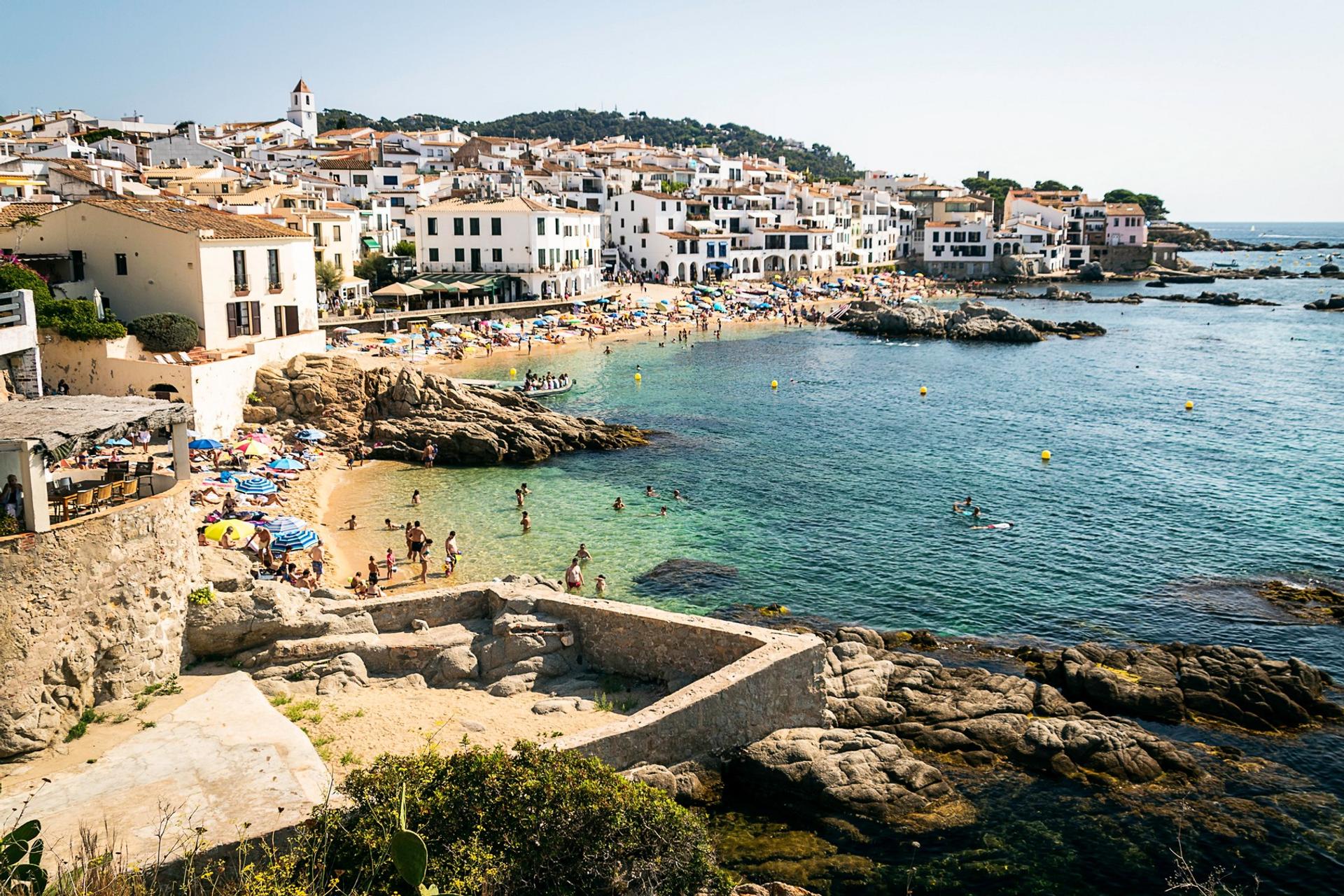 Beach with a lot of people and architecture in Calella de Palafrugell on a day with cloudy weather