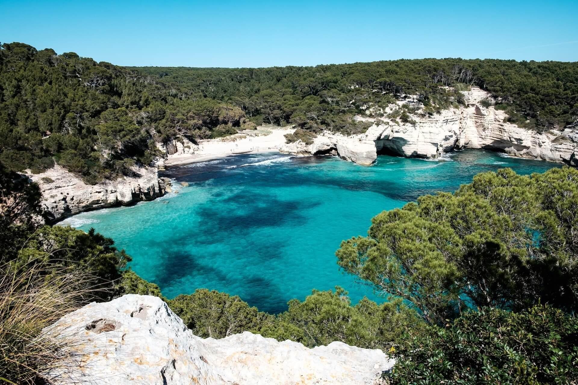 View of turqoise sea and and rock cliffs with trees in Menorca