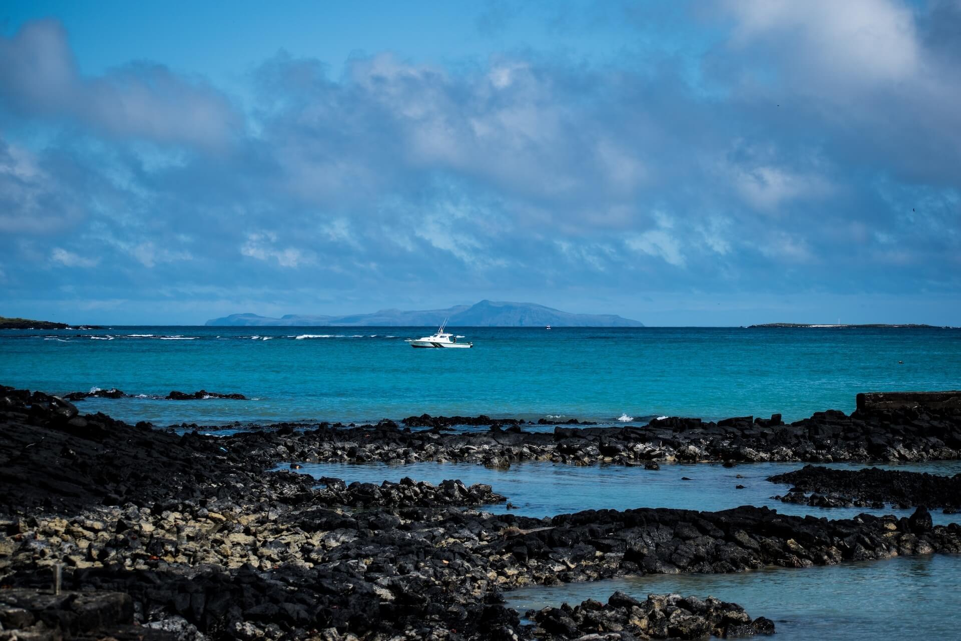 A boat sailing on a sea next to volcanic rocky formations with an island in the background